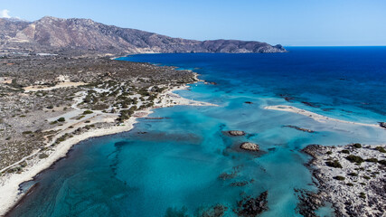 Fototapeta premium Aerial drone views of Elafonissi Beach reveal its stunning pink sand, turquoise waters, and shallow lagoons. The unique coastline, seen from above, highlights the vivid contrast between land and sea