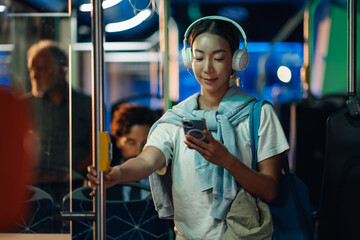 Obraz na płótnie Canvas Young woman using smartphone and listening music on bus at night
