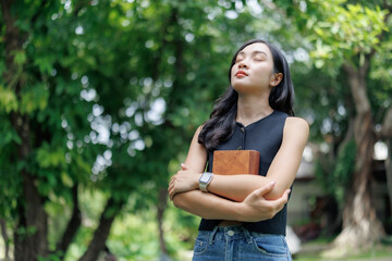 Fototapeta premium Young woman breathing fresh air and holding a book in a green park