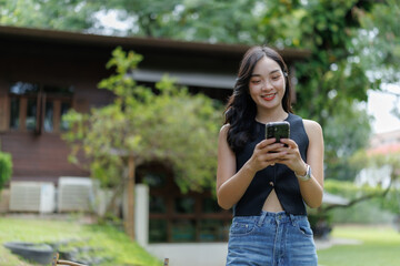 Fototapeta premium Young asian woman using smartphone in garden near wooden house