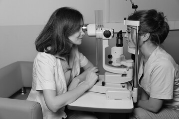 Female doctor examines young womans eye using professional vision testing equipment in clinic