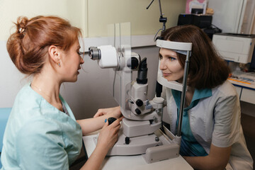 Female doctor examines young womans eye using professional vision testing equipment in clinic