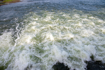 Rapidly flowing water with large waves over a dam on a river, water flow at the dam gate