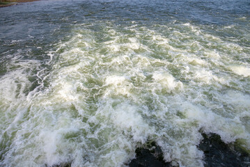 Rapidly flowing water with large waves over a dam on a river, water flow at the dam gate