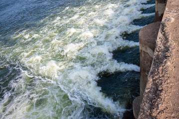 Rapidly flowing water with large waves over a dam on a river, water flow at the dam gate