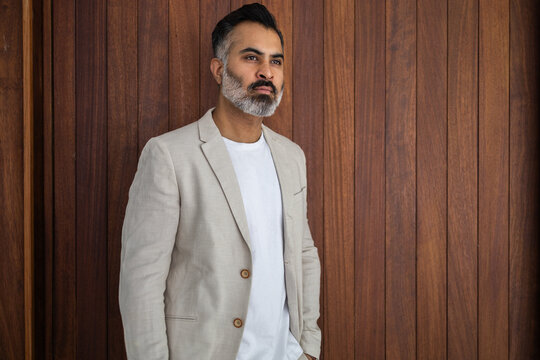 Indian man in beige blazer standing against wood panel - Powered by Adobe