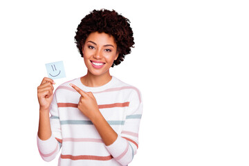 Photo of pretty dark curly skin lady holding in hands little paper emoticon directing finger what mood is better wear white striped pullover isolated pastel pink color background