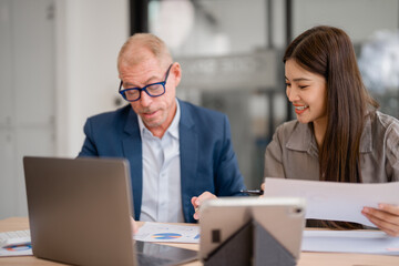 Senior businessman and young businesswoman are discussing charts and graphs using laptop and...