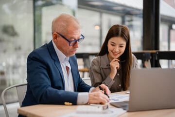 Senior businessman pointing at charts and graphs explaining to young businesswoman showing...