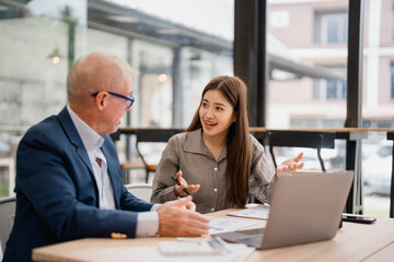 Two businesspeople are discussing strategy during a meeting using a laptop and documents in a...