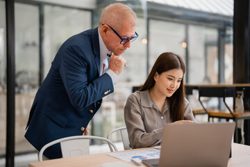 Senior manager coaching young asian businesswoman working with laptop and analyzing financial...