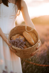 Woman holds basket of bread and flowers in lavender field at sunset