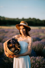 Woman wearing a straw hat poses with a basket of baked goods in a lavender field at sunset