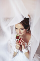 A bride is wearing a white dress and holding a red rose. She is looking at the camera with a smile...