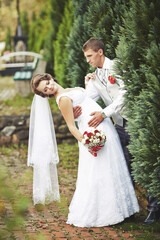 A bride and groom are posing for a picture in front of a tree. The bride is wearing a white dress...