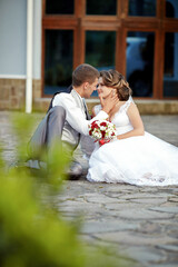 A bride and groom are sitting on the ground, with the bride holding a bouquet of flowers