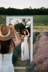 Woman in white dress admires herself in mirror surrounded by lavender fields at sunset