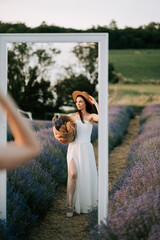 Woman in a white dress holding a basket in a lavender field during sunset