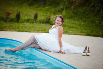 A woman in a white dress is sitting in a pool. She is smiling and wearing white shoes