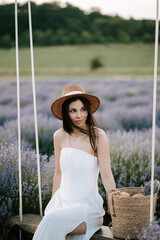 Woman in white dress sitting on swing surrounded by lavender fields at sunset