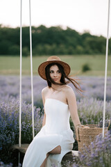 Woman in a white dress relaxing on a swing in a lavender field during golden hour