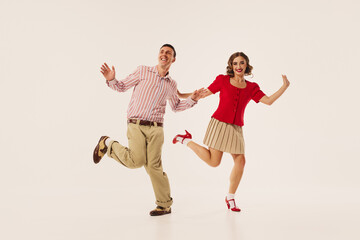A couple joyfully performs a retro lindy hop dance on a white background, wearing vintage attire....