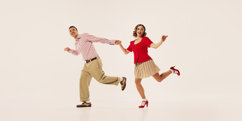 A couple joyfully performs retro lindy hop dance on a plain background, dressed in vintage attire....