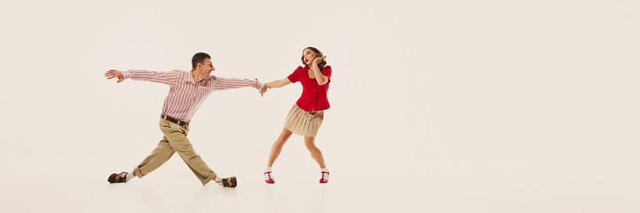 A couple joyfully performs retro lindy hop dance in vintage fashion against a plain background....