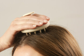 Girl doing herself a head massage using a scalp massager, stimulating hair growth,...