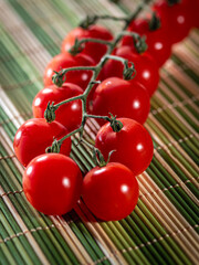 A bunch of red tomatoes are sitting on a bamboo mat