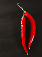 Two red chili peppers are shown on a black background