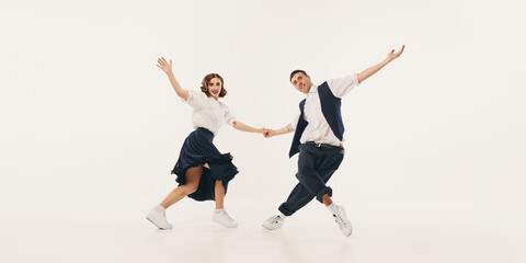 Two people joyfully performs the lindy hop dance in retro-inspired outfits against a neutral...