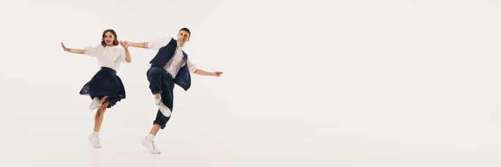 A dynamic duo performs lindy hop dance with lively retro flair against a minimalist backdrop....