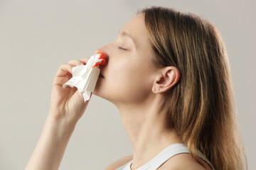 Nosebleed, a young woman with a bloody nose. Healthcare and medical concept. Close up studio image.