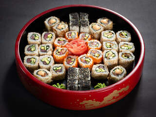A red bowl of assorted sushi is displayed on a black background