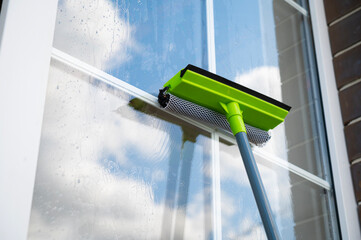 Washing windows in the house outside. Wet mop on the window glass with reflection of blue sky and clouds. Clean house concept.