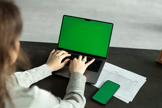 Woman typing on a laptop with a green screen at a desk
