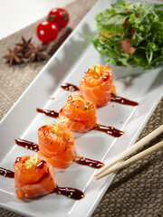 A plate of sushi with a sauce and a side of salad