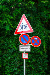 Bright german pedestrian crossing and no parking traffic signs with lush green foliage