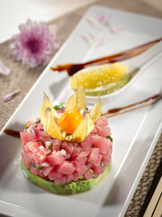 A plate of chopped tuna and guacamole with a pinkish color and a garnish of a yellow fruit