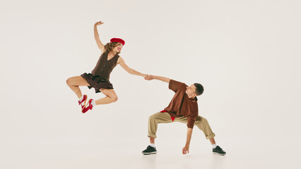 Energetic lindy hop dancers perform a high jump in vintage-inspired attire against a neutral backdrop. Concept of retro dance enthusiasm and spirited expression.