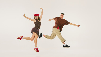 Energetic retro dancers perform a lindy hop routine, wearing vintage outfits, on a neutral...