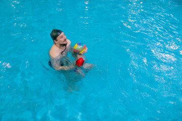 Happy middle-aged father swimming with cute adorable baby in swimming pool. Smiling dad and little child, boy having fun together. Active family spending leisure and time in spa hotel. Concept of kids