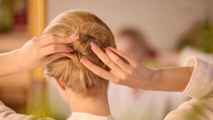 Fototapeta premium Clean-lazy hybrid. Caucasian woman styles an elegant bun using her delicate hands in a warmth-tinted setting. Concept of personal grooming and hairstyling techniques.