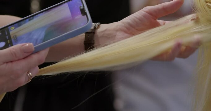 A hairstylist shows how to apply hair extensions with precision, using a smartphone to document the process. The elegant salon in Paris adds to the sophisticated atmosphere of the session.