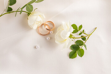 Gold wedding rings and white roses on satin backdrop