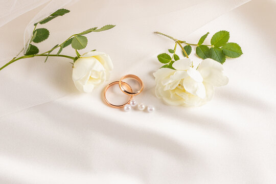 Gold wedding rings on satin with roses and pearls