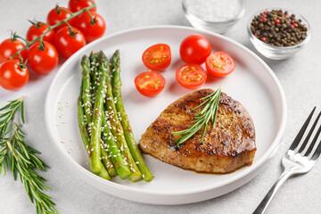 Close up, macro of tasty grilled beef steak served with green asparagus and cherry tomatoes on white plate, with cutlery. Perfect for food menu, diet, or culinary design concepts.