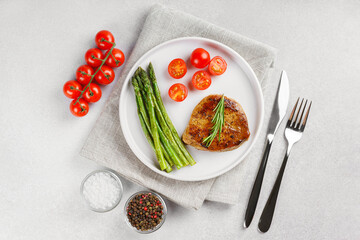 Tasty grilled beef steak served with green asparagus and cherry tomatoes on white plate, with cutlery and spices. Perfect for food menu, diet, or culinary design concepts.