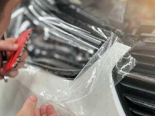The process of installing a protective polyurethane film for paint on the front headlight of a car. PPF is a polyurethane film that helps protect glass and metal from scratches. Selective focus.  